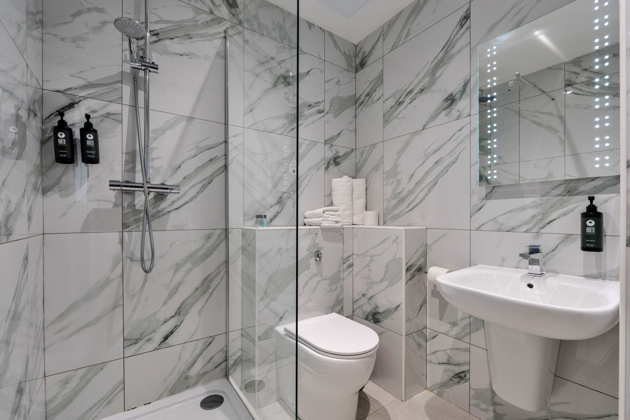 Une salle de bain moderne équipée d’une douche, de toilettes, d’un lavabo et d’un miroir avec éclairage.