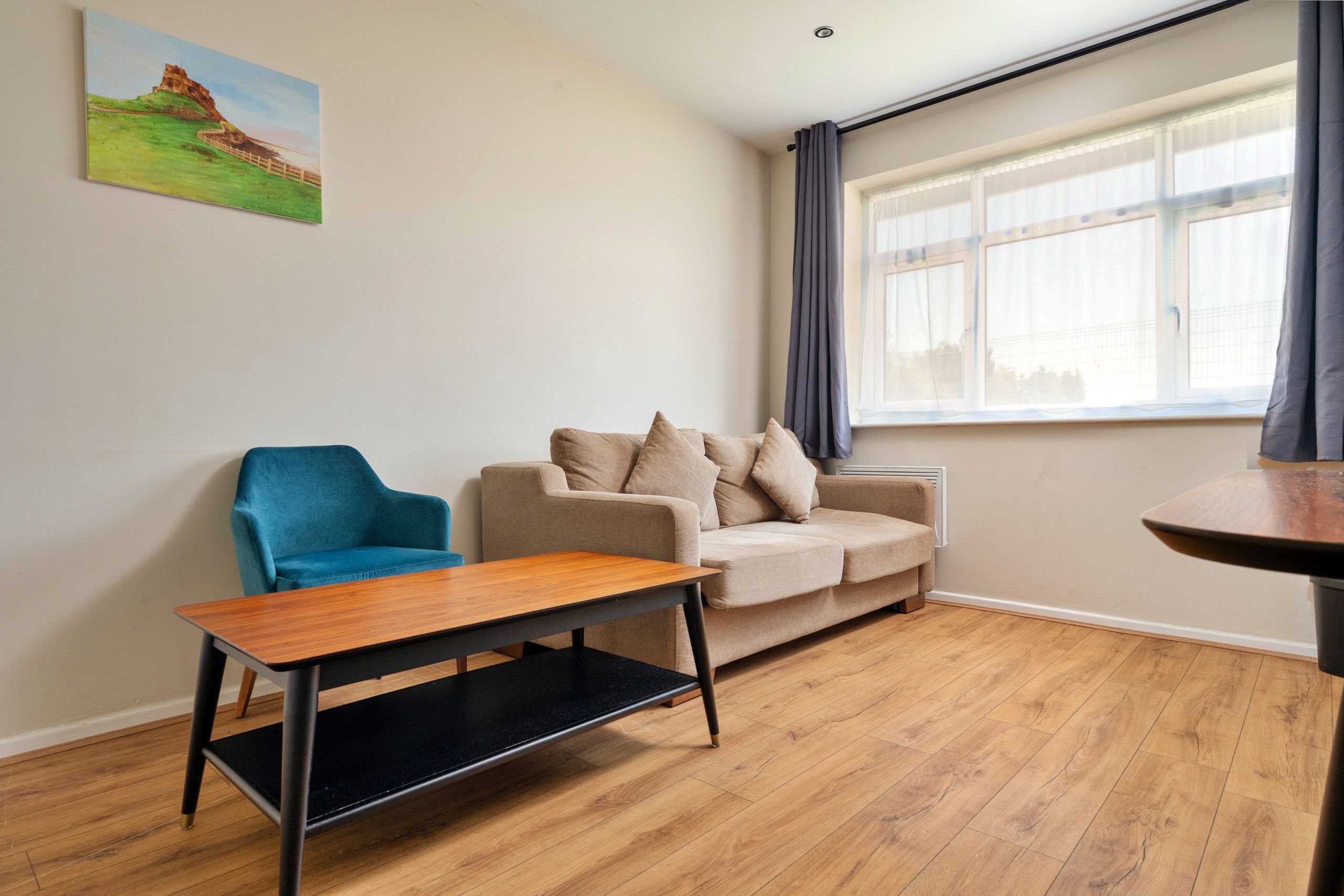 Una sala de estar moderna con un sillón azul, un sofá color beige con cojines, una mesa de centro de madera y una ventana con cortinas.