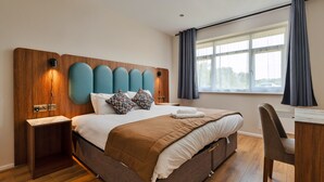 Ett modernt hotellrum med en stor säng, ett skrivbord och ett fönster med gardiner.