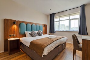 A modern hotel room with a large bed, a desk, and a window with curtains. - Park Hall, 2 Bedroom Apartment (Charnock Richard)
