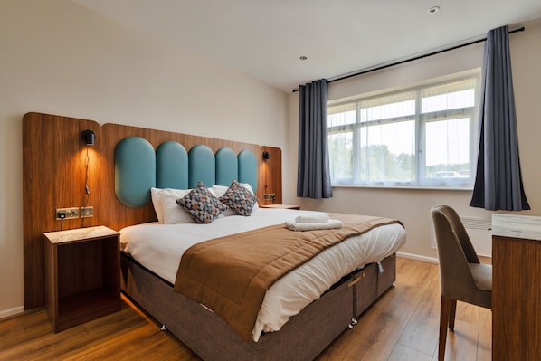 A modern hotel room with a large bed, a desk, and a window with curtains.