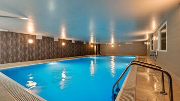 Una piscina interior con superficie de agua azul cristalina, rodeada de paredes con textura y luces empotradas.