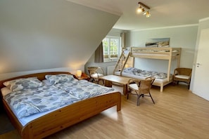 A room with a wooden bed, a bunk bed, a table with chairs, and a window. - Holiday home with 4 bedrooms (Blekendorf)