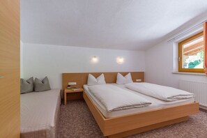 A single bedroom with a wooden bed, a nightstand, two wall-mounted lights, and a window with blinds. - Holiday apartment with 1 bedroom (Schwendau)