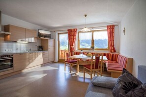 A modern kitchen with wooden cabinets, a dining area with a table and chairs, and a sofa. - Holiday apartment with 1 bedroom (Schwendau)
