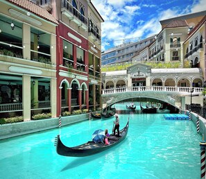 A canal with gondolas, a bridge, and buildings with balconies and shops. - Park McKinley West Tower-A Japanese Inspired Cozy Quiet 1BR Condo 85"HDTV 穏やかな (Taguig)