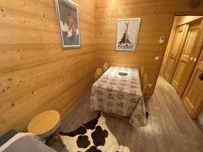 Una stanza piccola con pareti in legno, un letto con copriletto a motivi cardi, un tavolo rotondo in legno e un tappeto in pelle di mucca.