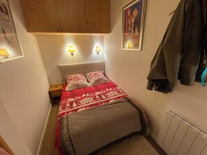 Una camera da letto con un letto, due lampade a parete, un cappotto appeso e un quadro sulla parete.