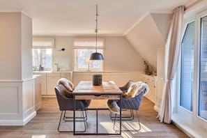 Ein Essbereich mit einem Holztisch, zwei Stühlen mit Fellkissen, einer Pendelleuchte und Blick ins Freie durch ein großes Fenster.