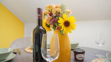A dining table with a wine bottle, a glass, a vase with flowers, and a jar of jam.