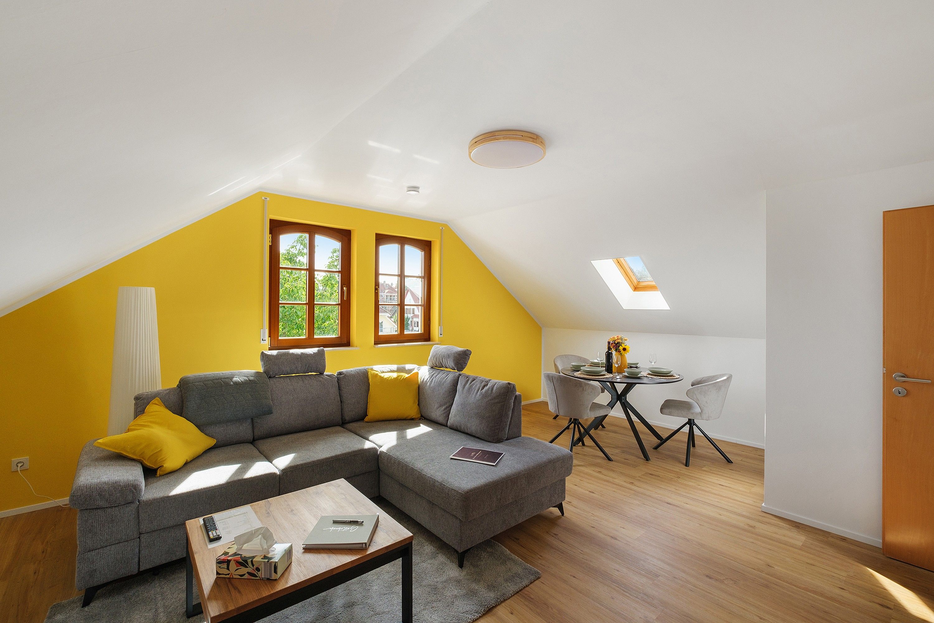 Un espace de vie moderne doté d’un plafond en pente, d’un canapé d’angle, d’une table à manger avec des chaises et d’un petit coin cuisine.