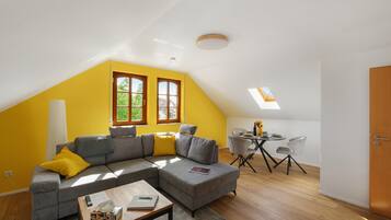 Un espace de vie moderne doté d’un plafond en pente, d’un canapé d’angle, d’une table à manger avec des chaises et d’un petit coin cuisine.