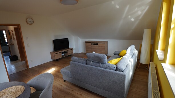 A modern living room with a grey sofa, a flat-screen TV, wooden flooring, and a yellow accent wall. - Honeygreen Apartment in Bodenheim with Pool, Terrace, and Wi-Fi (Bodenheim)