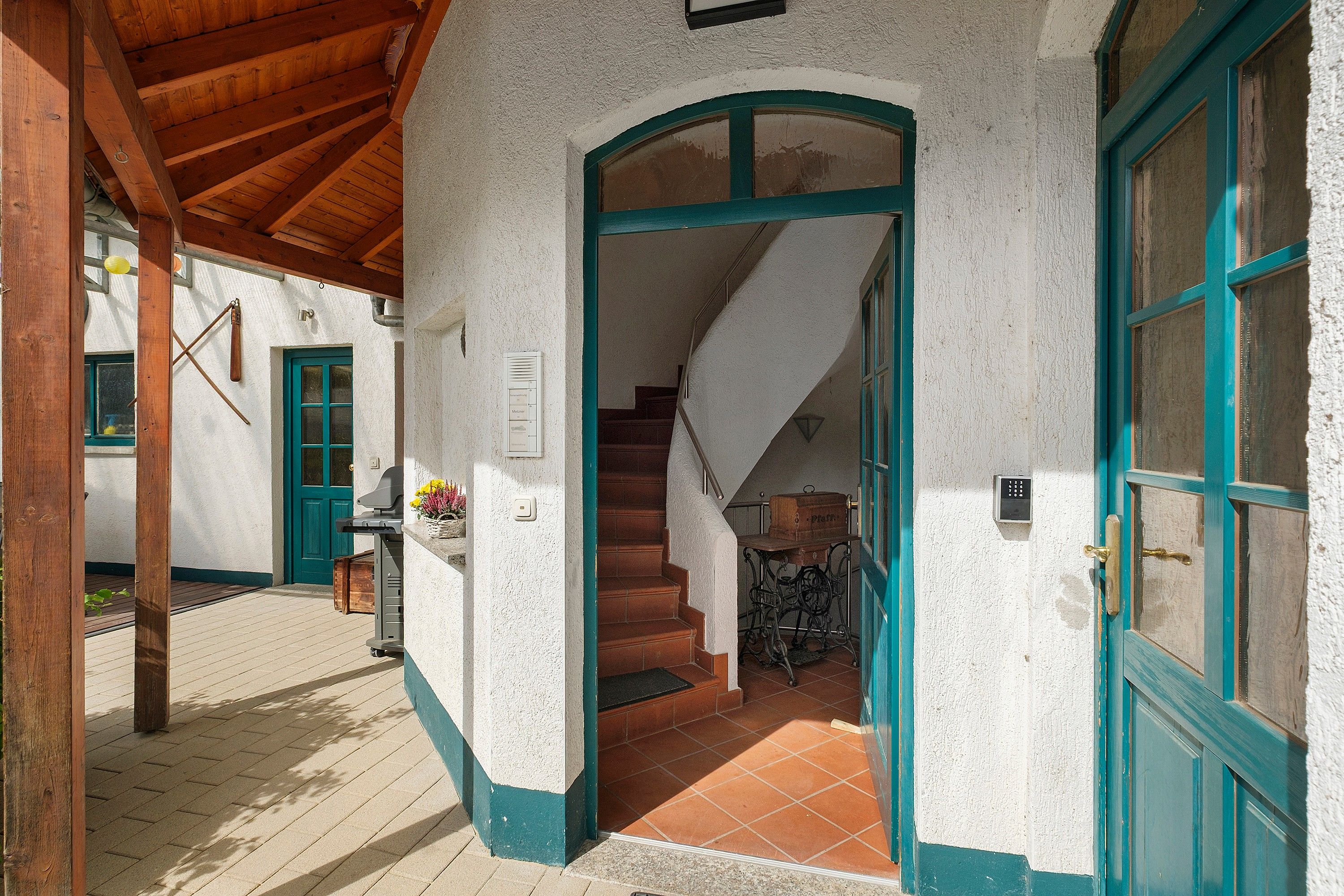 A traditional building with a wooden staircase leading to an upper level, a green door, and a white wall with a textured finish.