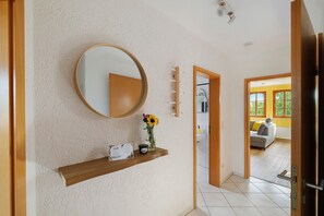 A hallway with a wooden shelf holding a welcome card, a candle, and a vase with flowers.