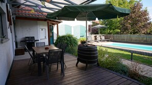 An outdoor patio with a wooden table and chairs, a grill, and a pool area with umbrellas. - Honeygreen Apartment in Bodenheim with Pool, Terrace, and Wi-Fi (Bodenheim)