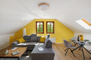 A modern living room with a sectional sofa, a dining table with chairs, and a skylight.
