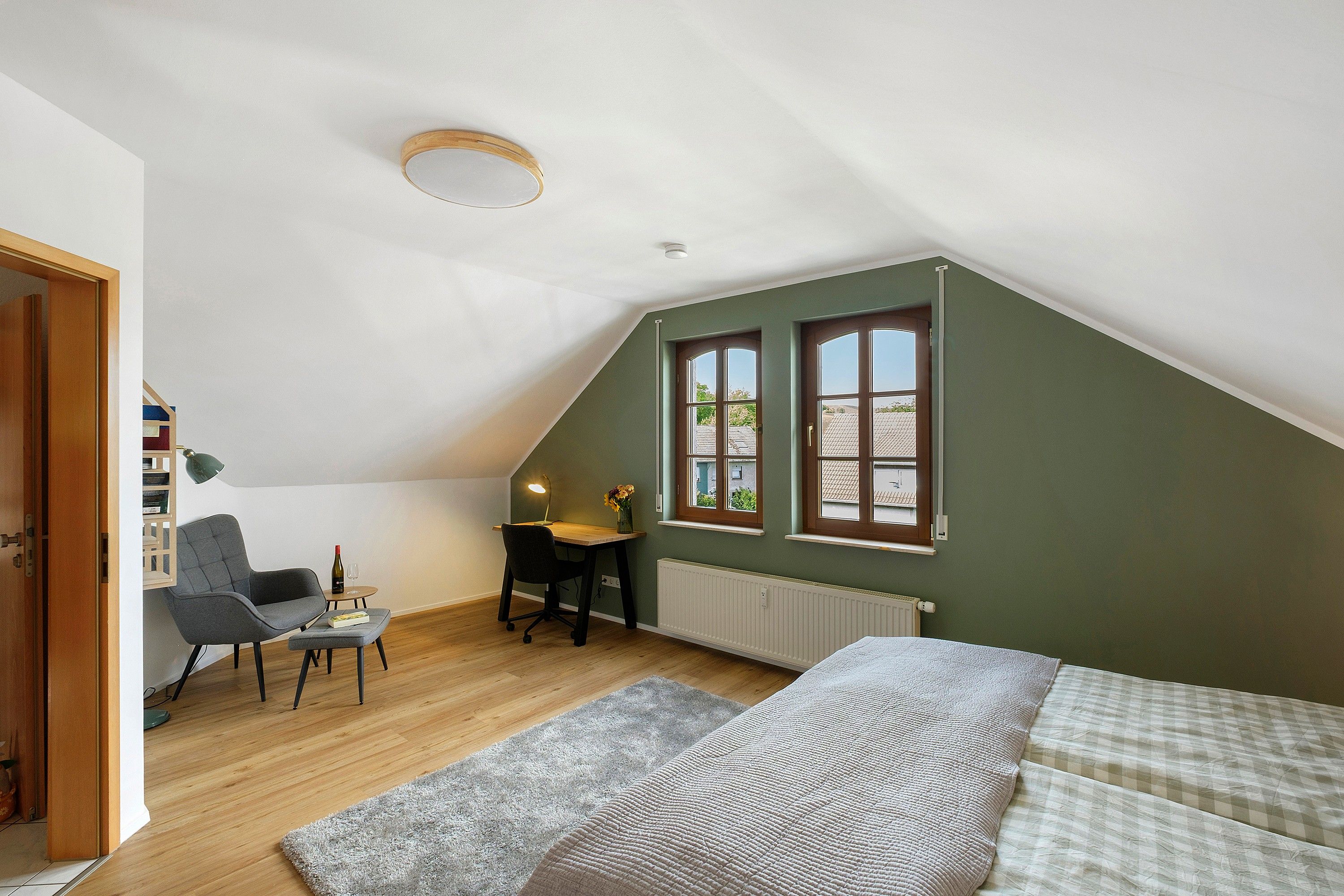 Ein Zimmer mit schrägem Dach, einem Schreibtisch mit Stuhl, einem Bett und einem Fenster mit Blick.