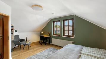 Ein Zimmer mit schrägem Dach, einem Schreibtisch mit Stuhl, einem Bett und einem Fenster mit Blick.