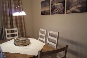 Ein Essbereich mit einem Tisch für zwei Personen, weißen Stühlen, einem gewebten Korb und einer weißen Tischdecke.