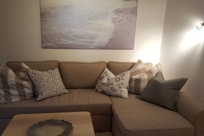 Ein beiges Sofa mit floralen und karierten Kissen, ein Holztisch mit einer Dekoration und ein Strandbild an der Wand.