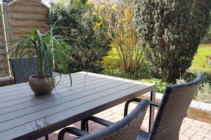 Eine Terrasse im Freien mit Tisch und Stühlen, umgeben von Pflanzen und einem Holzzaun.