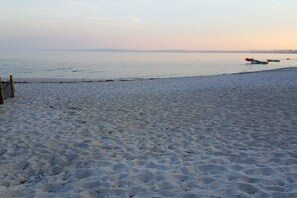 Ein sandiger Strand mit ruhiger See, einigen Booten und einer entfernten Küstenlinie.