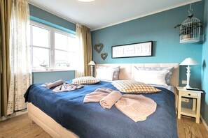 Een slaapkamer met een bed, twee nachtkastjes, een raam met gordijnen en decoratieve wandversiering.