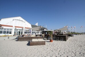 Ein Gebäude direkt am Strand, genannt 'Strandhalle', mit Außenbestuhlung und einem Blumentopf.
