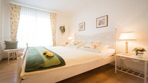 Un lit bien fait, avec des oreillers et un plaid vert, une table de chevet avec une lampe, une chaise et une fenêtre avec des rideaux.