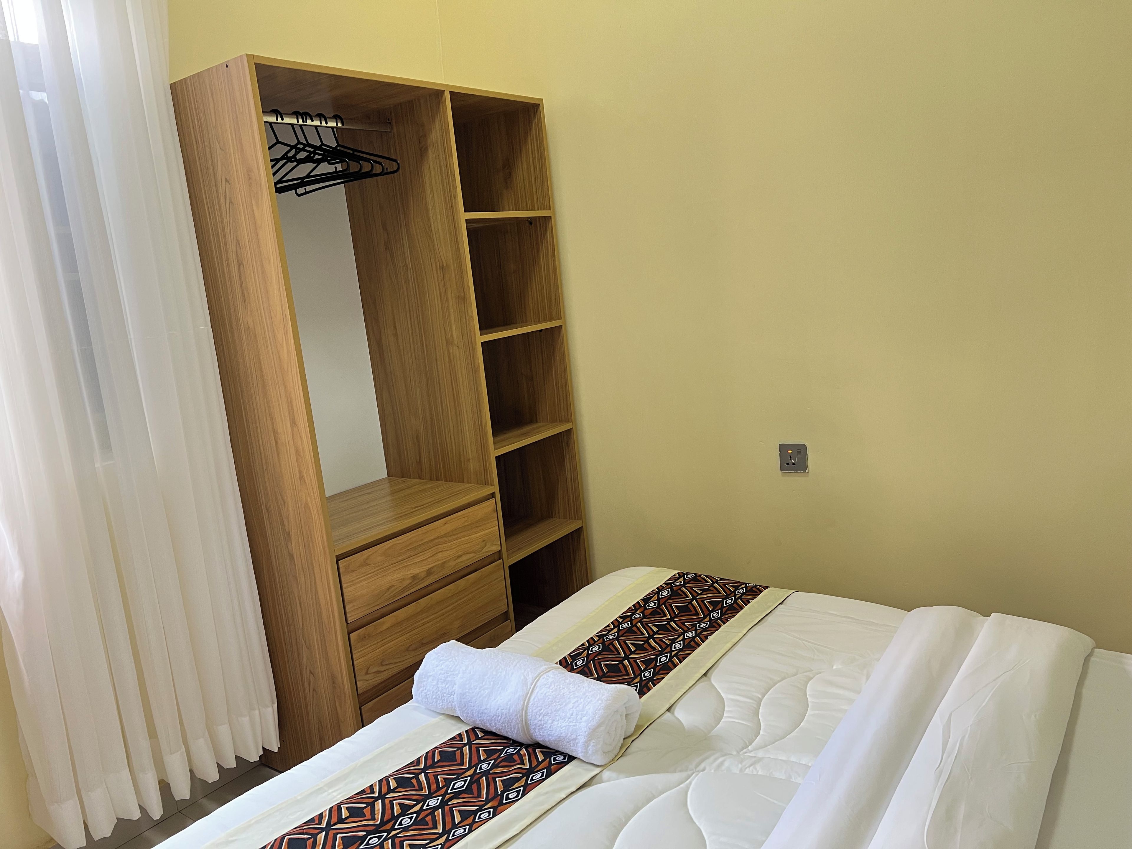 A hotel room with a bed, a wooden wardrobe, a mirror, and a wall socket.