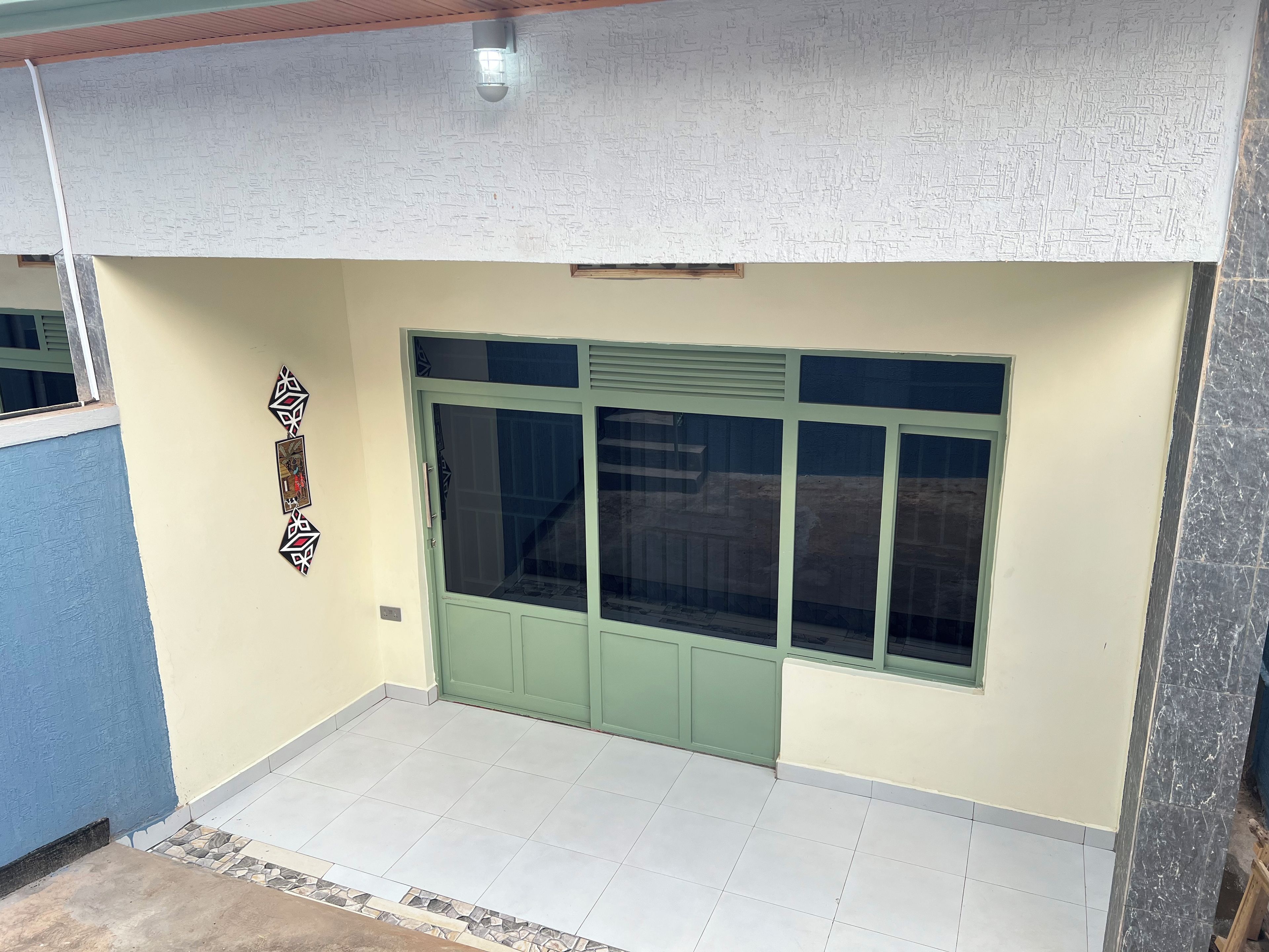 Una habitación con puerta verde, piso de baldosas y una lámpara fijada a la pared.