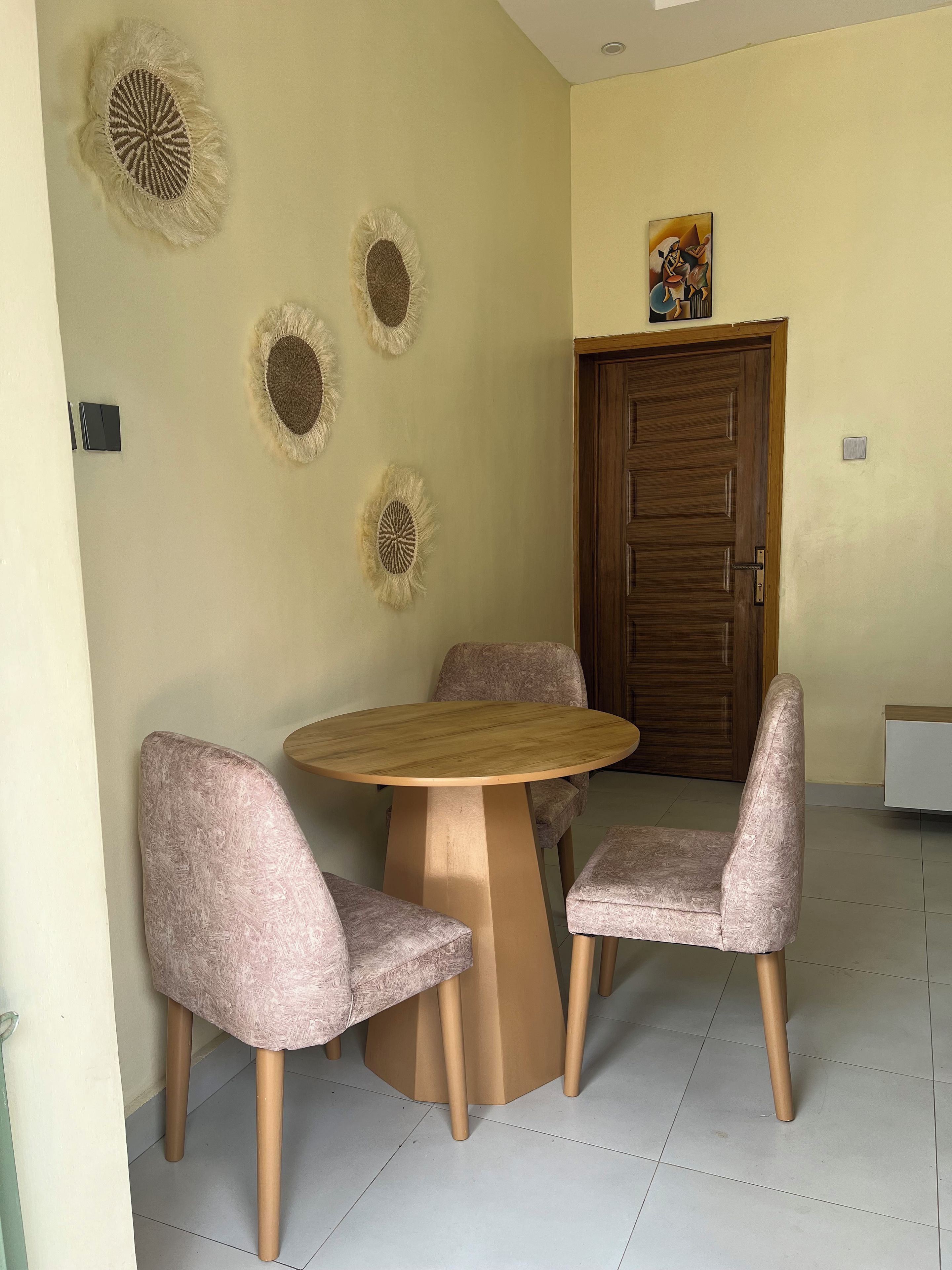 Un comedor con una mesa redonda y cuatro sillas, una puerta de madera y decoración en la pared.
