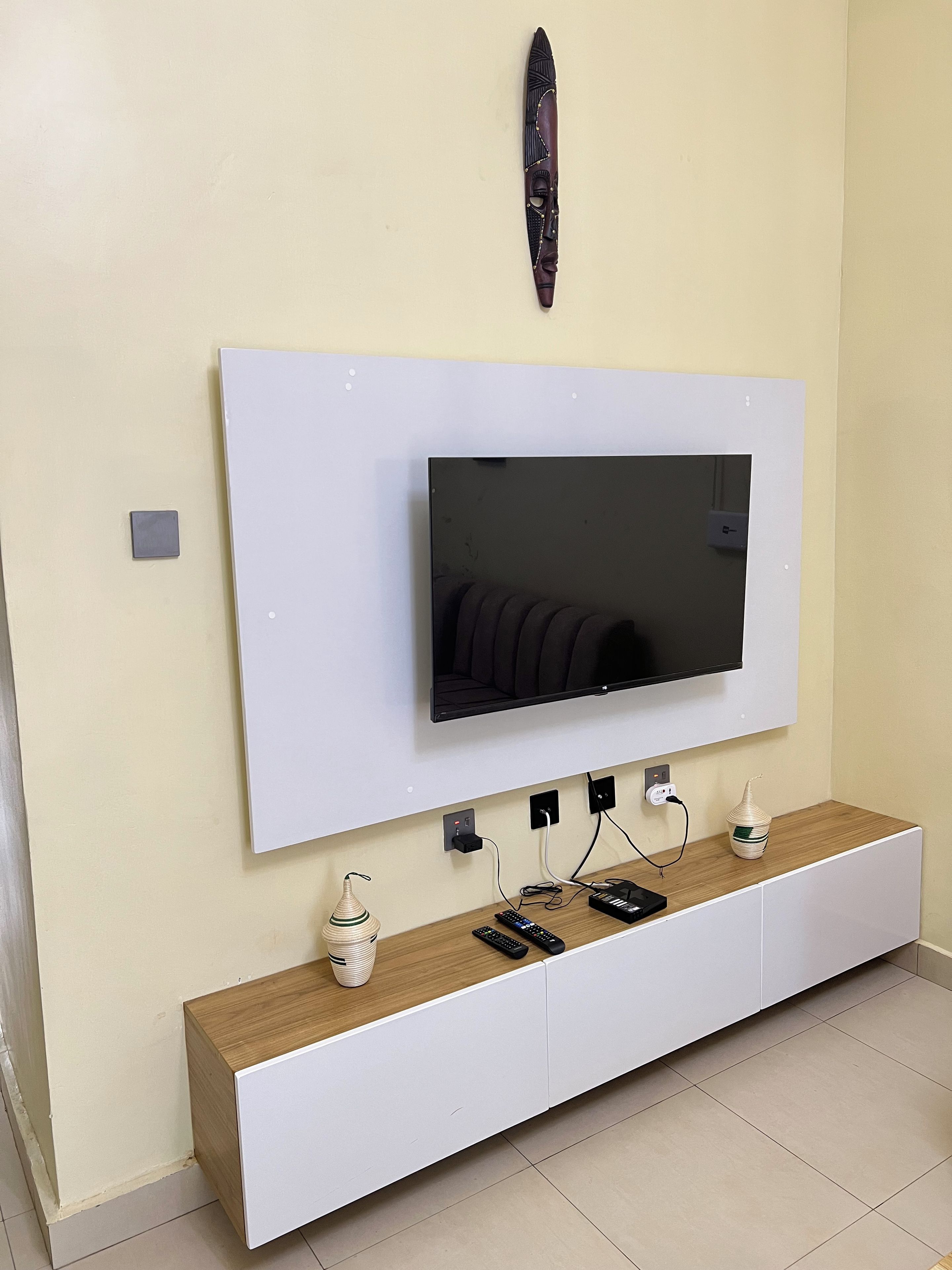 A modern living room with a mounted TV, white entertainment unit, and a decorative wall piece.