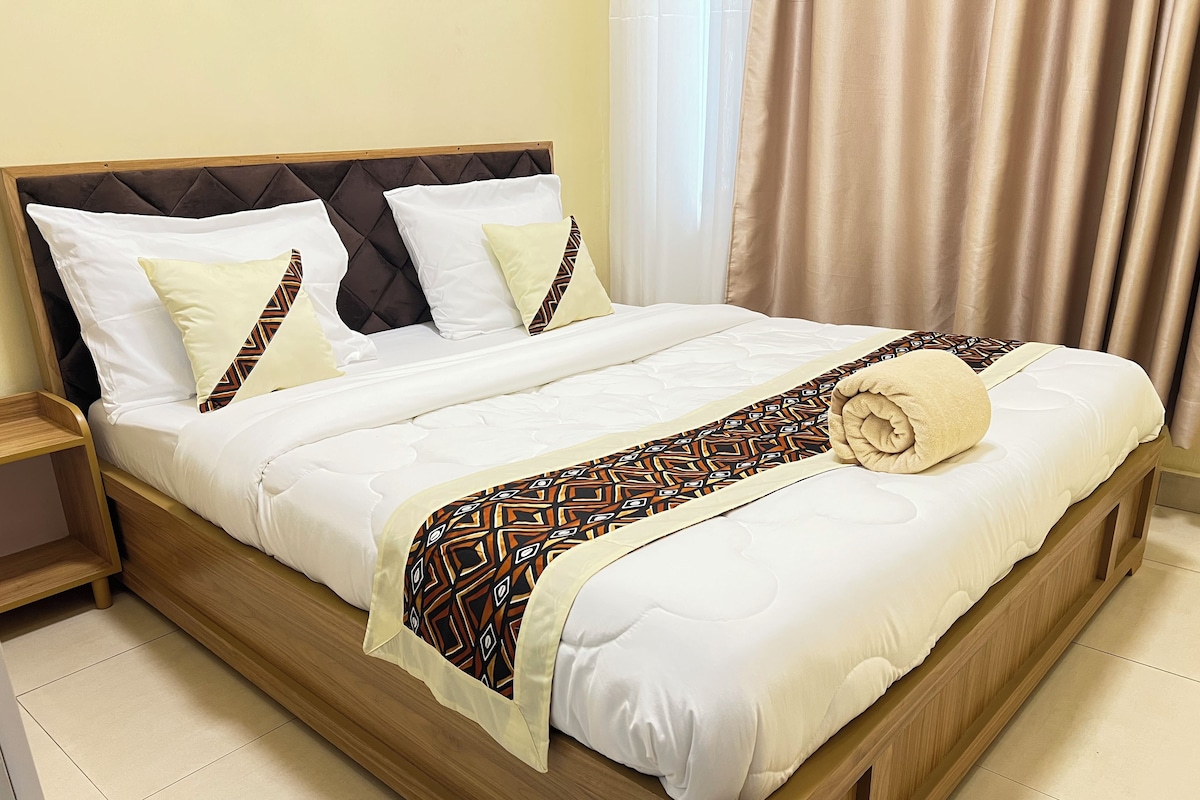A double bed with a patterned throw blanket, a rolled towel, and a wooden headboard.