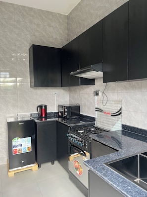 A modern kitchen with black cabinets, a gas stove, a coffee maker, and a refrigerator.