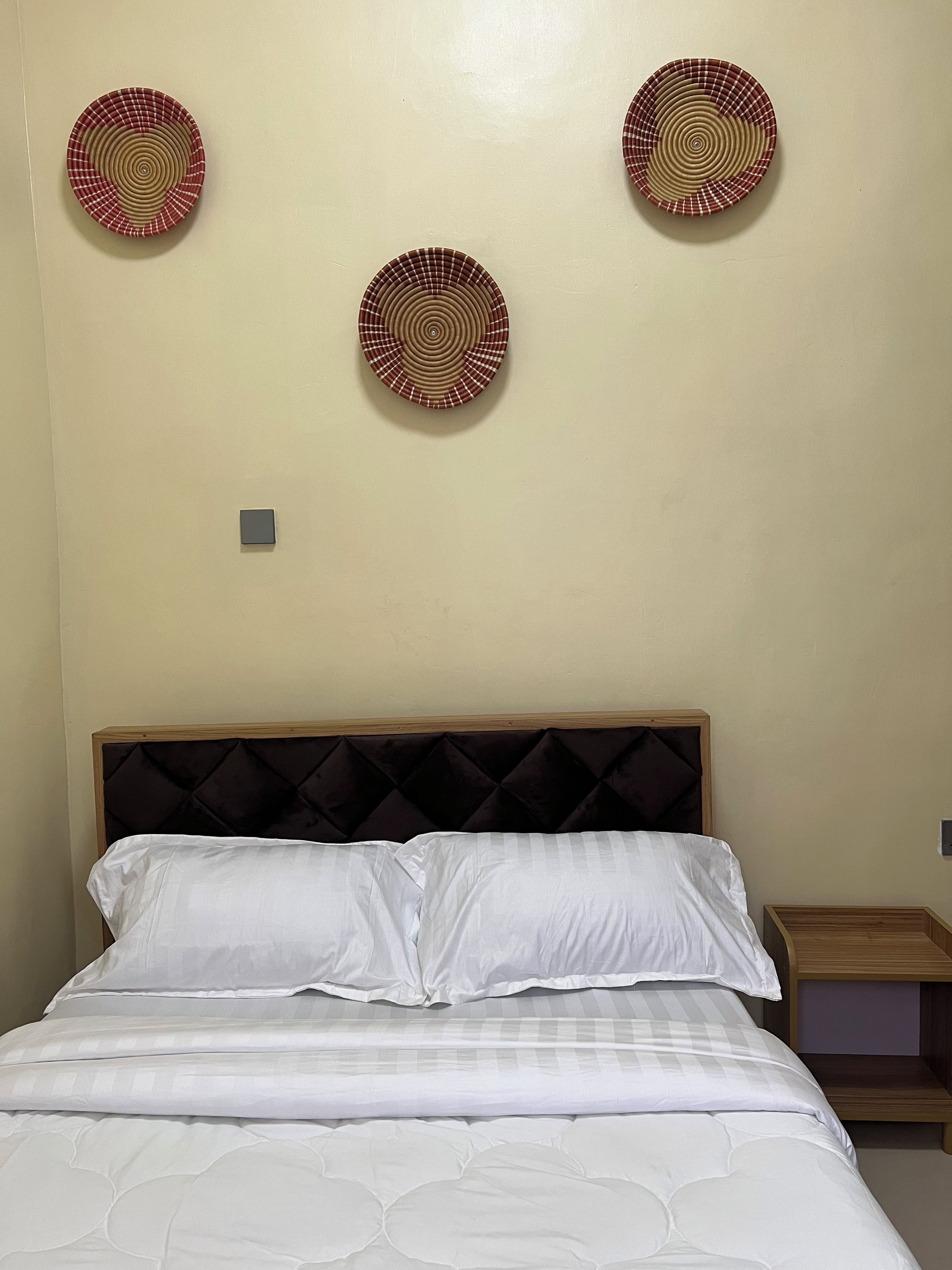 Una cama bien hecha con ropa de cama blanca y un cabecero oscuro, junto con tres platos decorativos colgados en la pared.