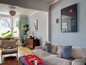 A living room with a sofa, a coffee table, a chair, a bookshelf, and a large window. - Spacious 1BDR Flat with Garden in Brockley (Greater London)