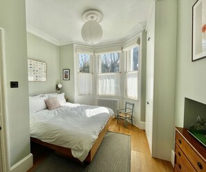 A bedroom with a large bed, a radiator, a chair, and a window with curtains. - Spacious 1BDR Flat with Garden in Brockley (Greater London)