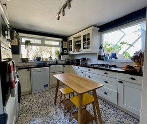 A kitchen with white cabinets, a wooden table, and a window with plants. - Spacious 1BDR Flat with Garden in Brockley (Greater London)