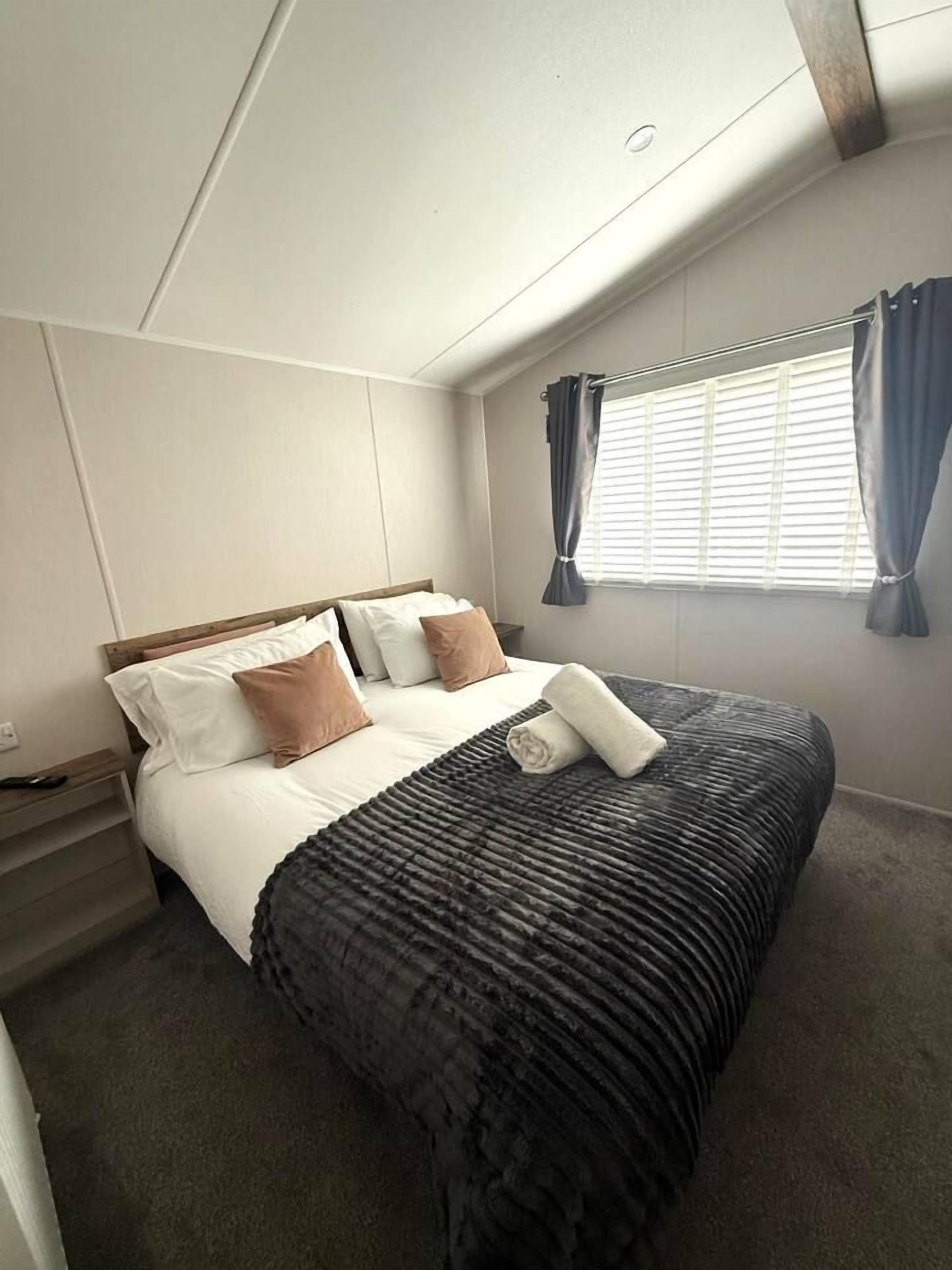 A hotel room with a bed, a nightstand, a window with curtains, and a ceiling with a light fixture.