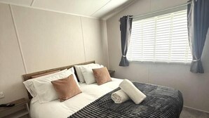 Habitación de hotel con cama, mesita de noche, ventana con cortinas y lámpara en el techo.