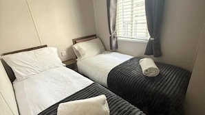 Habitación de hotel con dos camas individuales, una ventana con cortinas y una mesita de noche fijada a la pared.