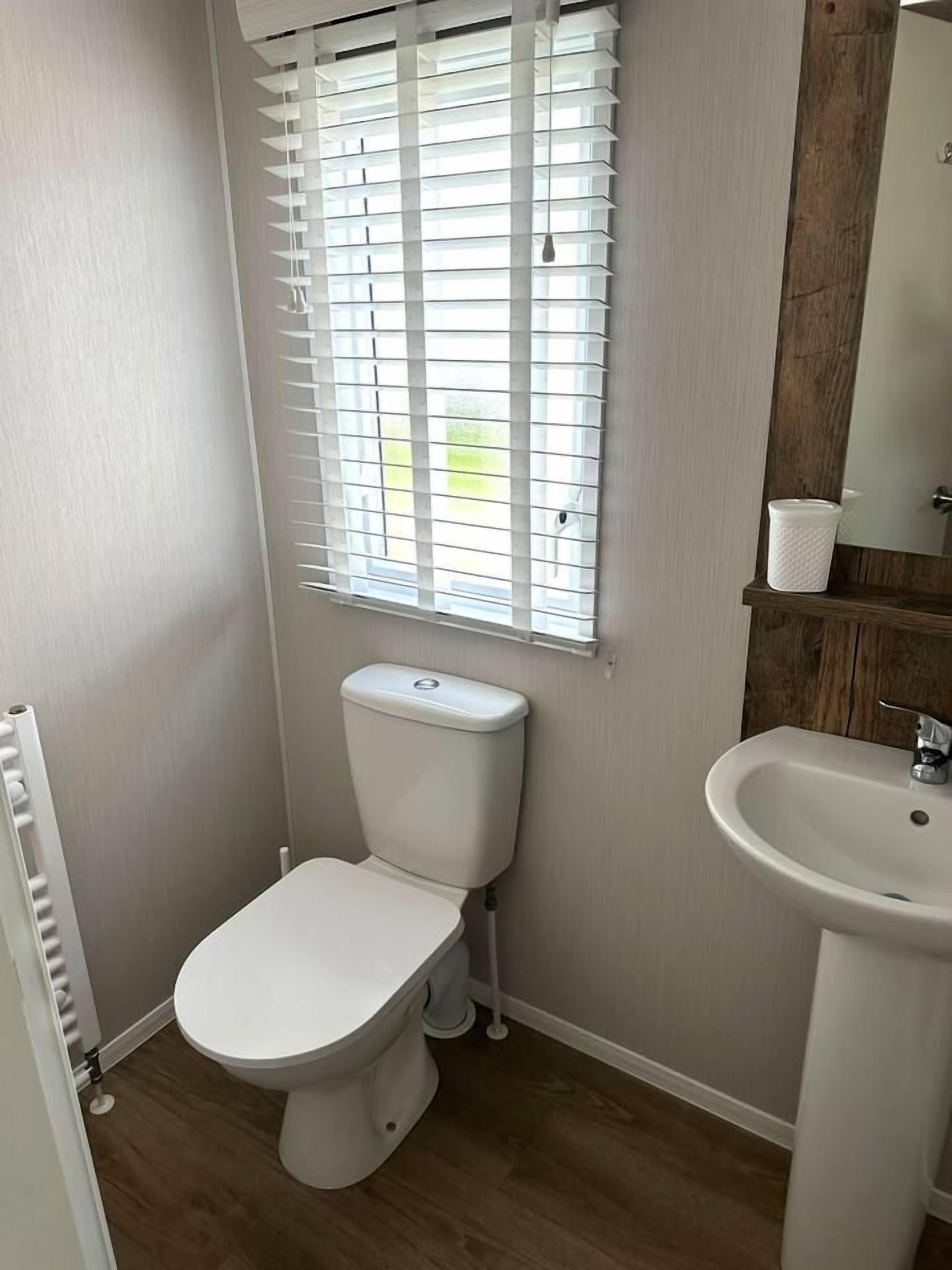 A compact bathroom with a toilet, a sink, and a window with blinds.