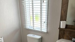 Un baño pequeño con inodoro, lavamanos y ventana con persianas.
