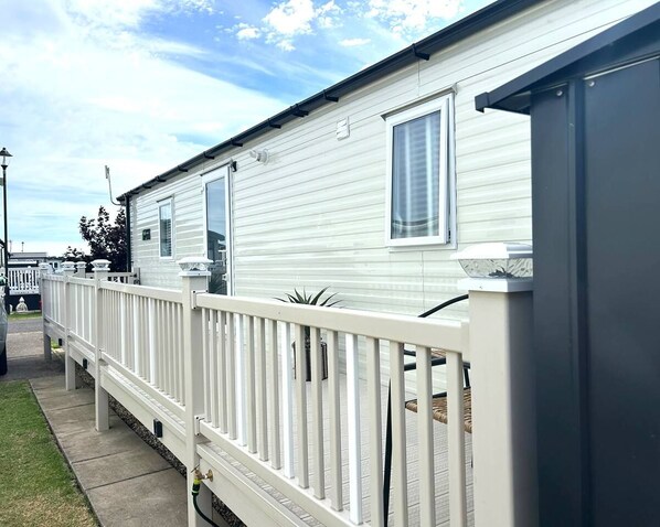 A mobile home with a white exterior, a fenced front yard, and a clear sky.
