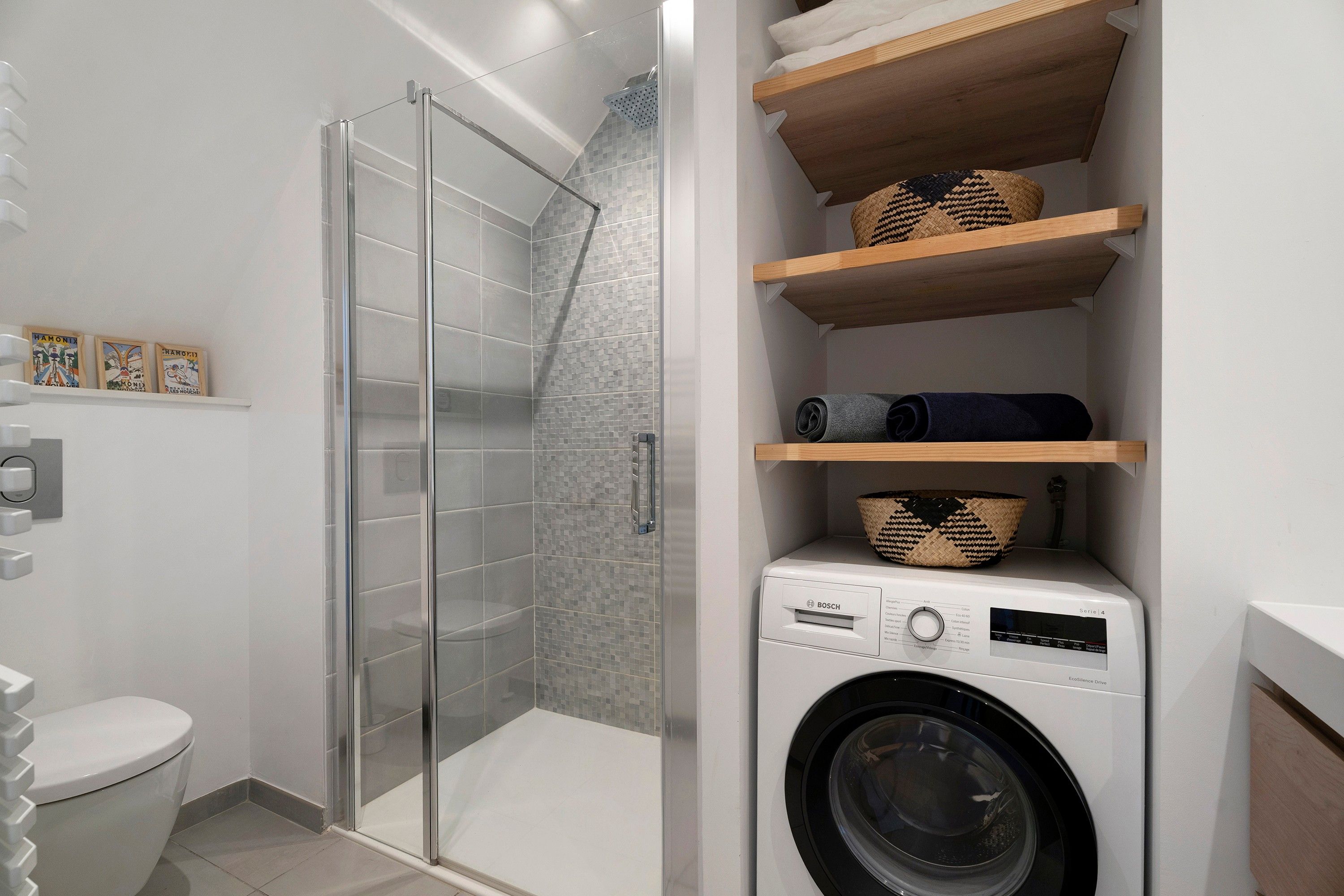 Ein modernes Badezimmer mit einer gläsernen Dusche, einer Waschmaschine von Bosch und Holzregalen mit Körben.
