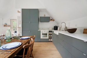 Een moderne keuken met grijze kastjes, een wit aanrechtblad en een houten eettafel voor vier personen.