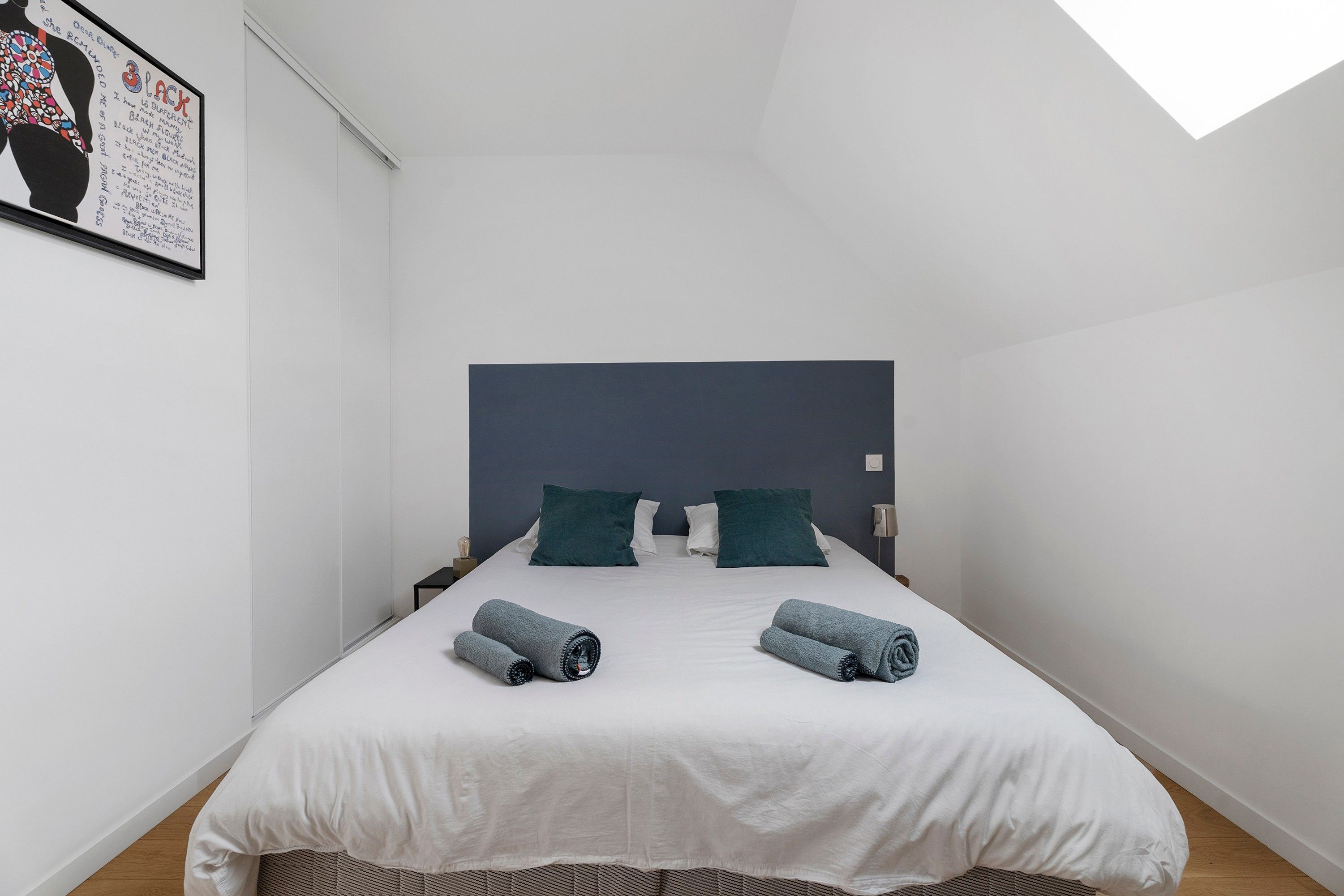 Une chambre d’hôtel avec un lit, deux oreillers, une tête de lit, une table de chevet et une œuvre d’art encadrée au mur.