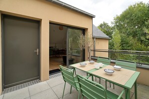 Een terras buiten met een eettafel, groene stoelen en een schuifdeur die leidt naar een binnen eetgedeelte.